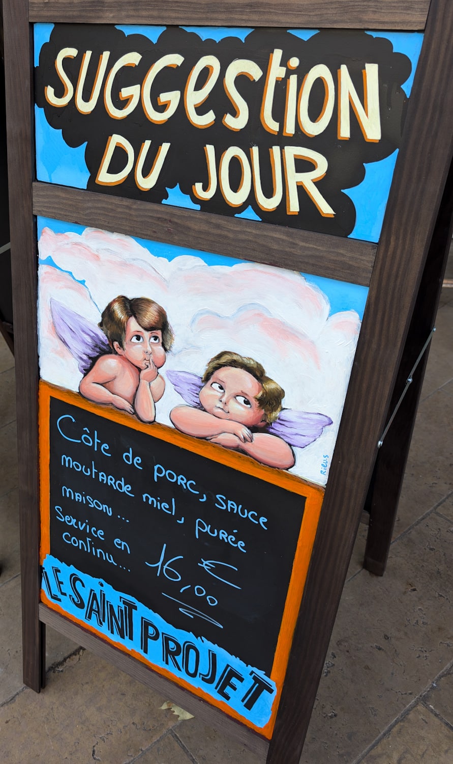 Ardoise menu du jour peinte Ă la main avec caricature d'un chef cuisinier souriant.