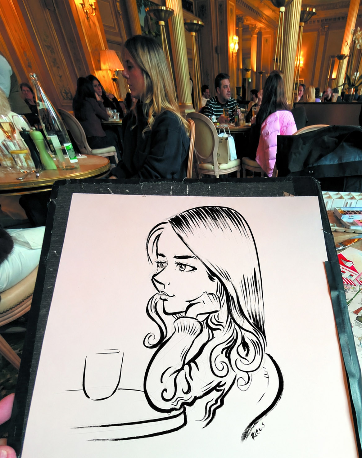 Au Café de la Paix, le modèle assis et son portrait à l’encre au premier plan