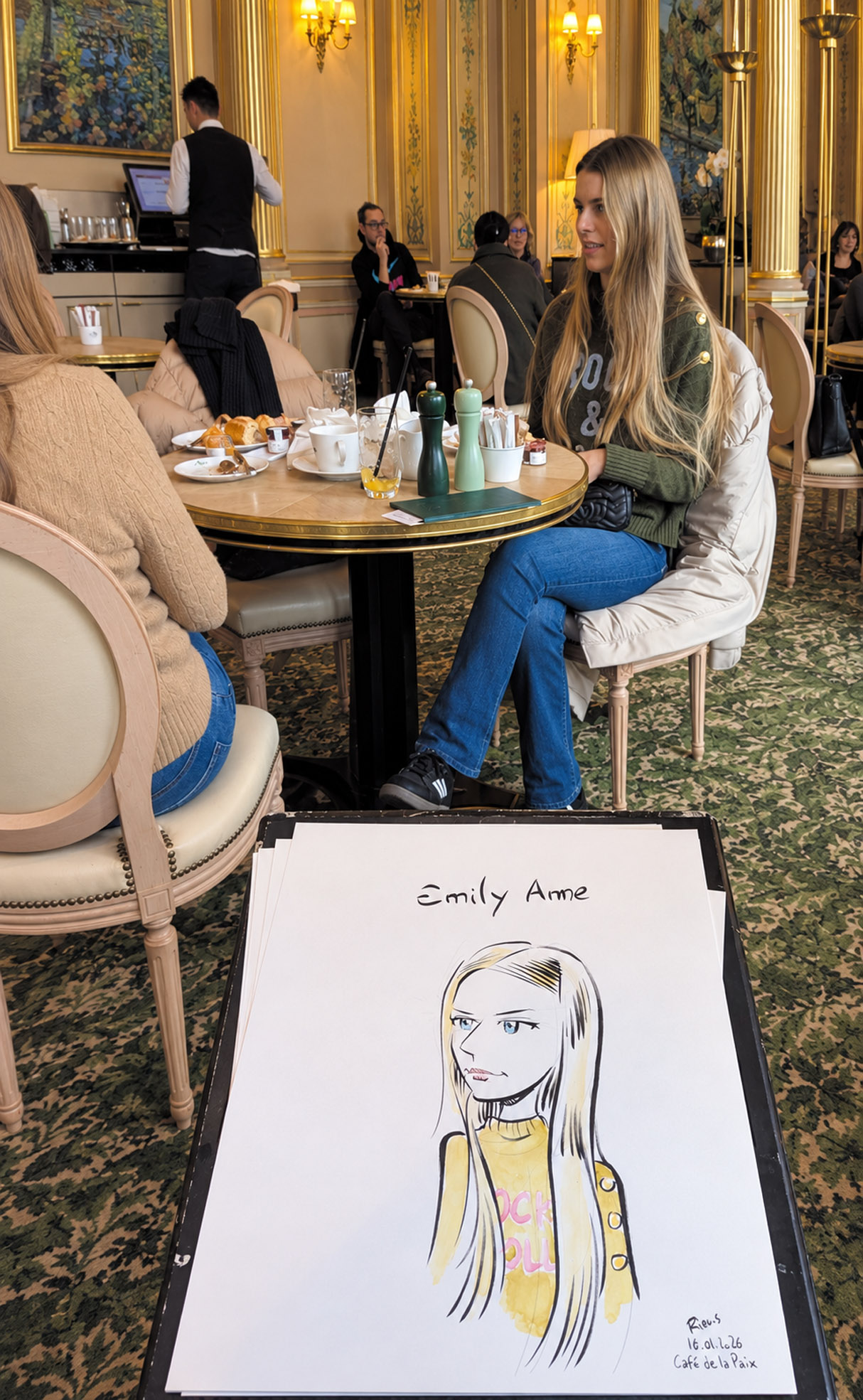 Une jeune femme pose au Café de la Paix avec son portrait en couleur au premier plan