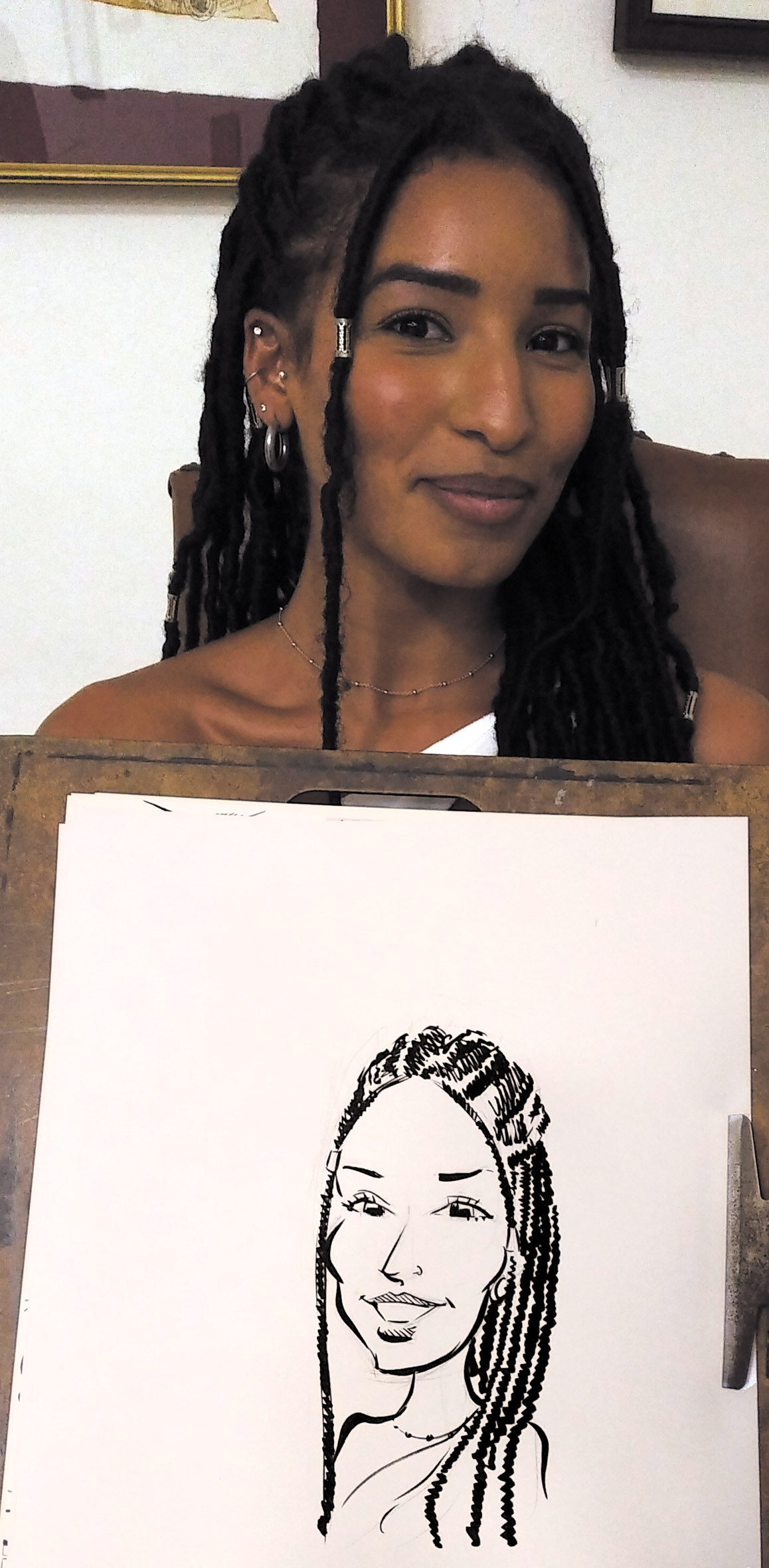 Une femme aux longues tresses tient son portrait à l’encre sur une grande feuille
